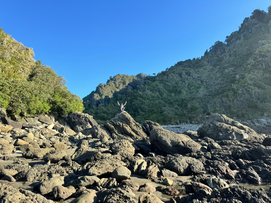 Man with hands in air at Ocean Beach, the destination of Wharekai Te Kou Walk in Jackson Bay, New Zealand