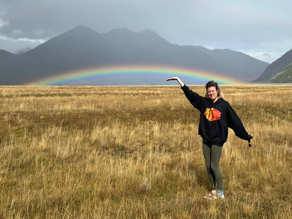 Woman enjoying low rainbow on the way to Hawdon Shelter Campgrounds in New Zealand