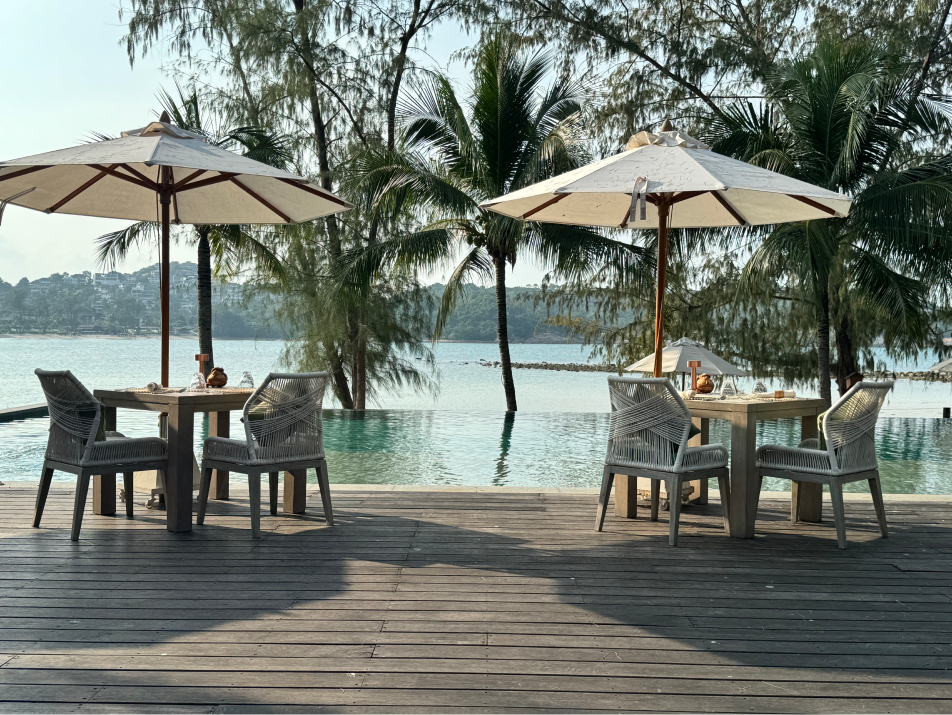 A view of Cape Fahn resort in Koh Samui, Thailand - tables with umbrellas, palm trees, and a pool that seems to connect directly to the ocean