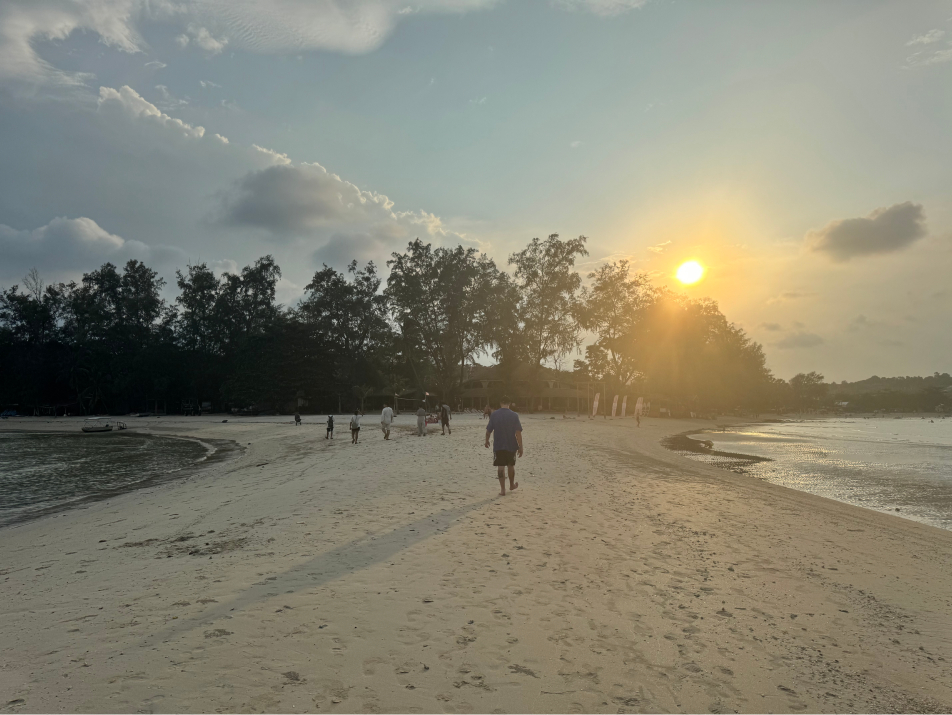 A man walking down a beach with 2 bodies of water on either side in Koh Samui, Thailand