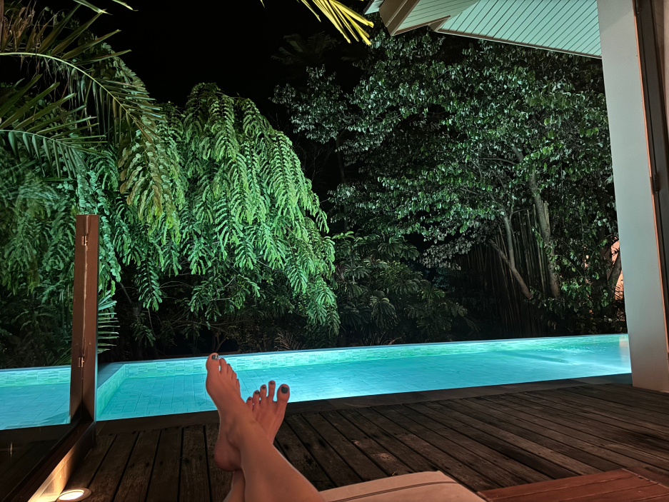 Feet in front of a private lit-up pool surrounded by green lushness at nighttime at Cape Fahn Resort on Koh Samui, Thailand