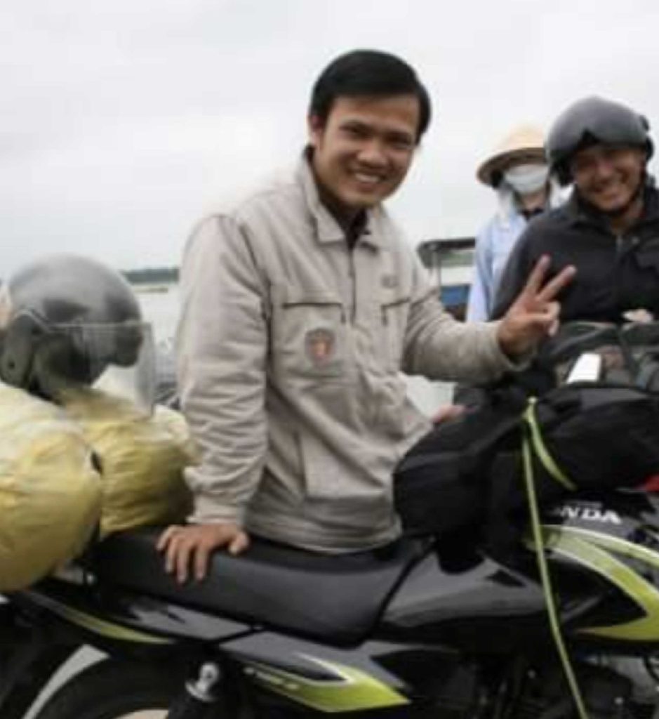 A Vietnamese man giving a peace sign next to a motorcycle in Vietnam