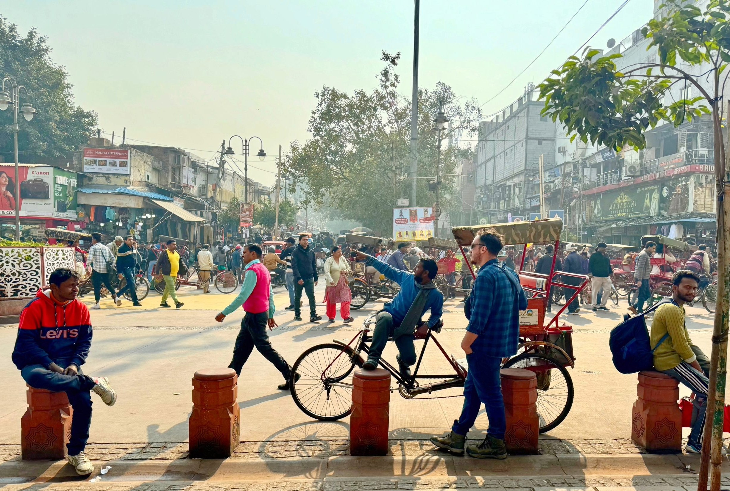 An Old Delhi scene - a local Indian man pointing upward to show a tourist something while sitting on his rickshaw with crowds of people around