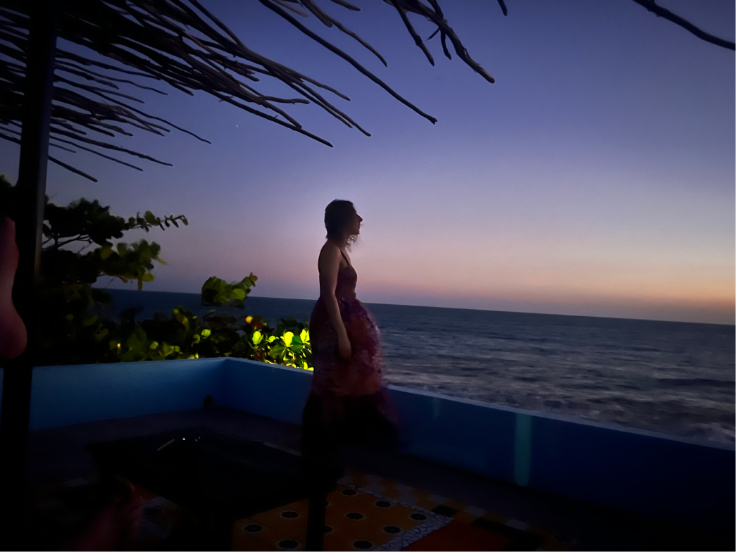 The side view of a woman standing on a roof deck admiring the ocean at dusk in Treasure Beach, Jamaica