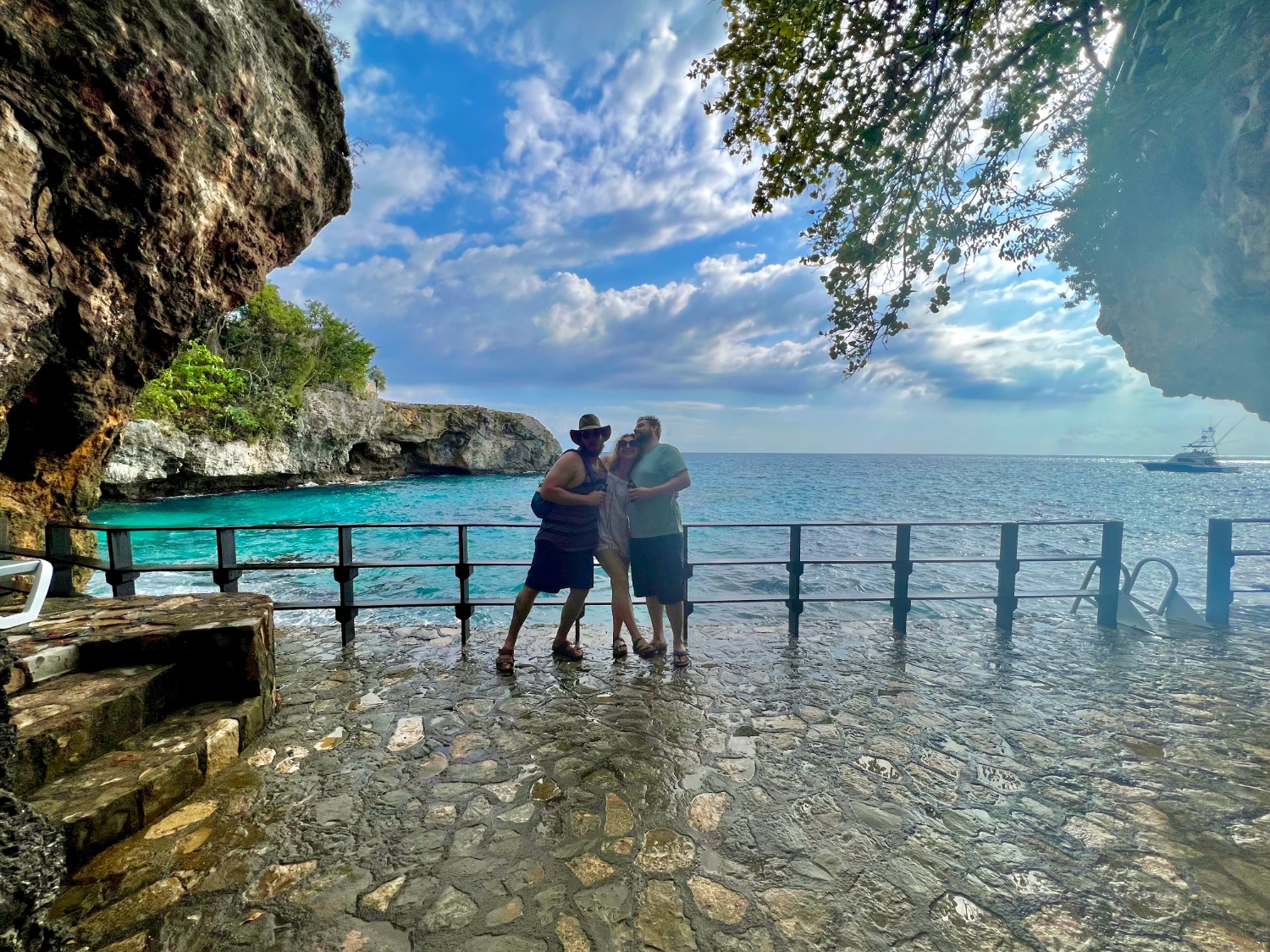 A woman in between 2 guys posing in front of the rocky cliffs and blue water of Negril, Jamaica