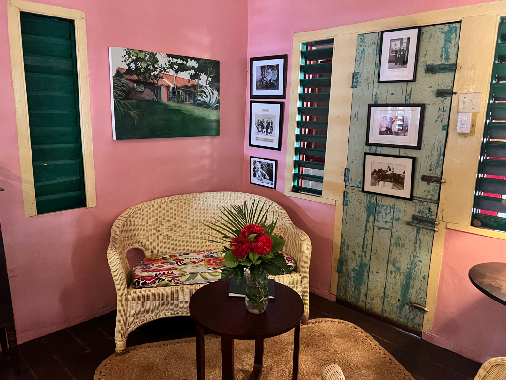 The cute corner of the lobby at Jakes hotel in Treasure Beach, Jamaica adorned with pink walls, green and yellow shutters, and a whicker couch