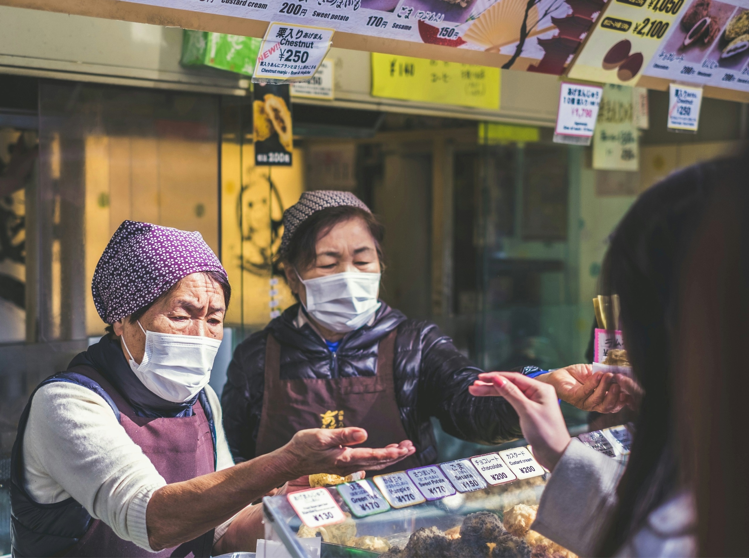 2 older Asian women with face masks on handing out treats to a younger woman