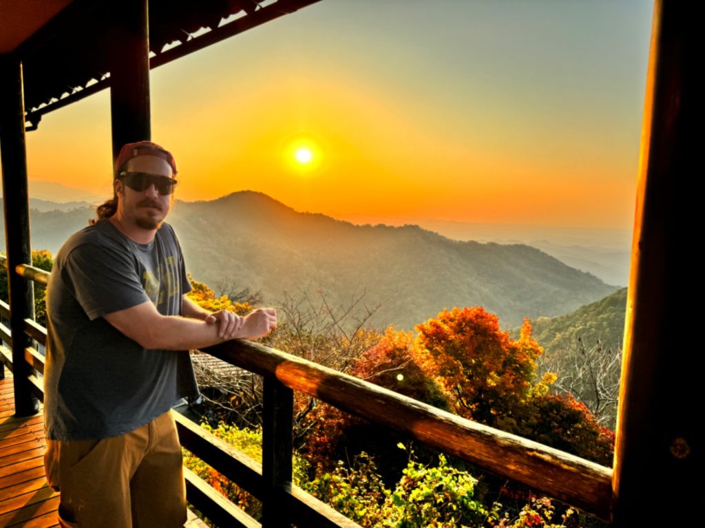 Man in front of stunning sunset and mountain view on the deck of Ikumo Lodge in Komatsu, Japan