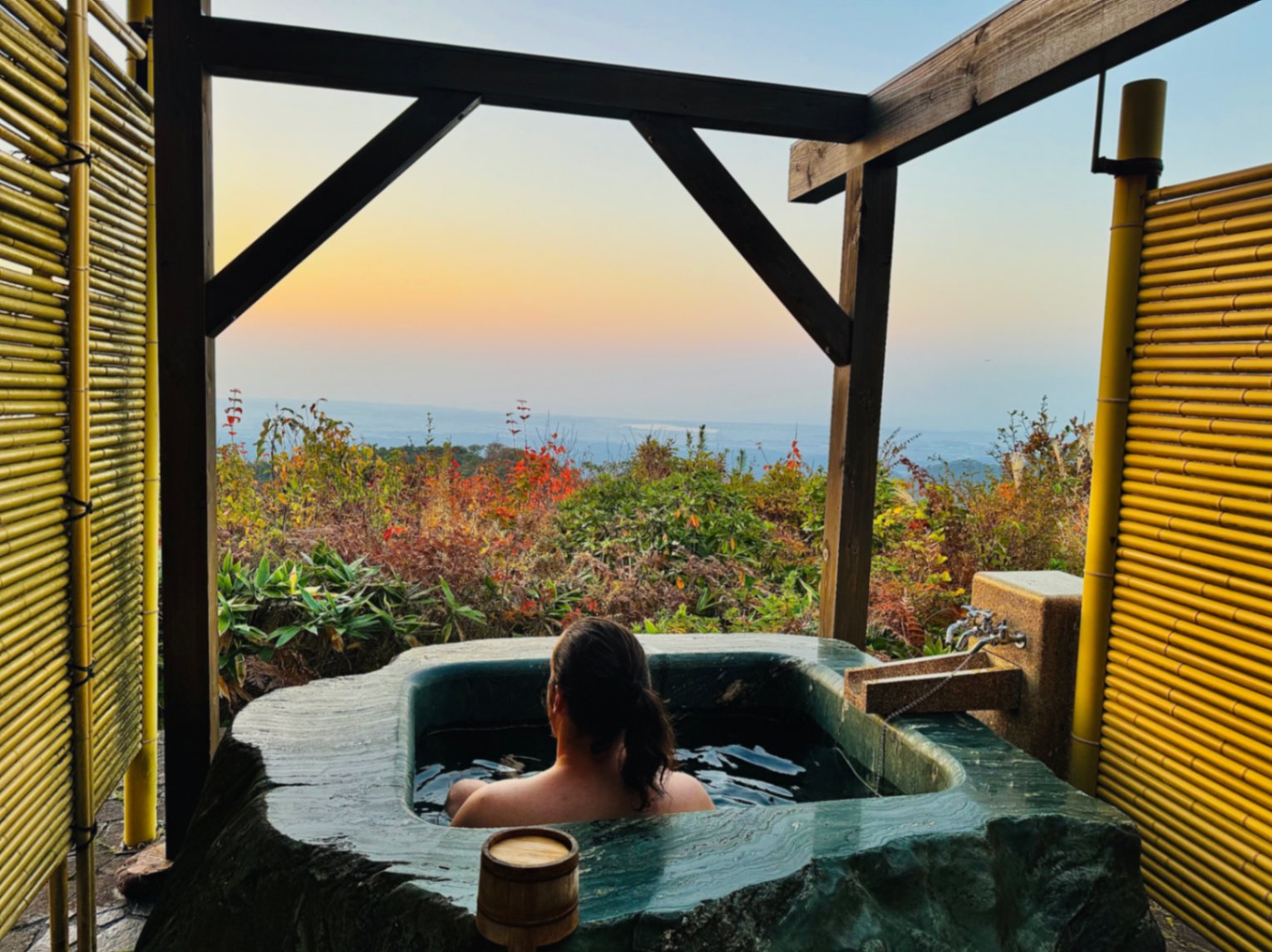 Man with ponytail soaking in private hot tub with sunset views from Ikumo Lodge in Komatsu, Japan