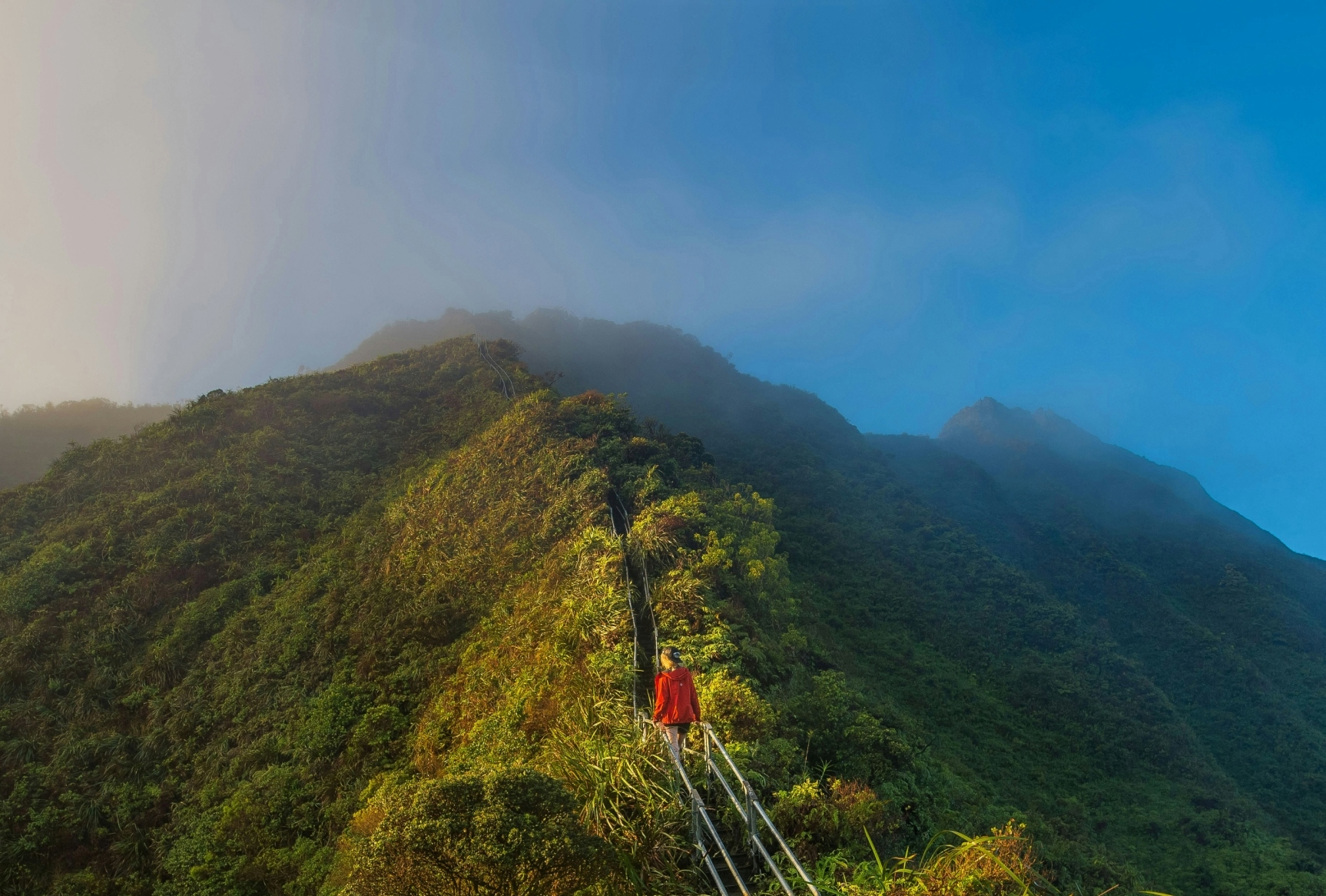 A woman ascending remote steps in the middle of lush green mountains and blue skies in the background