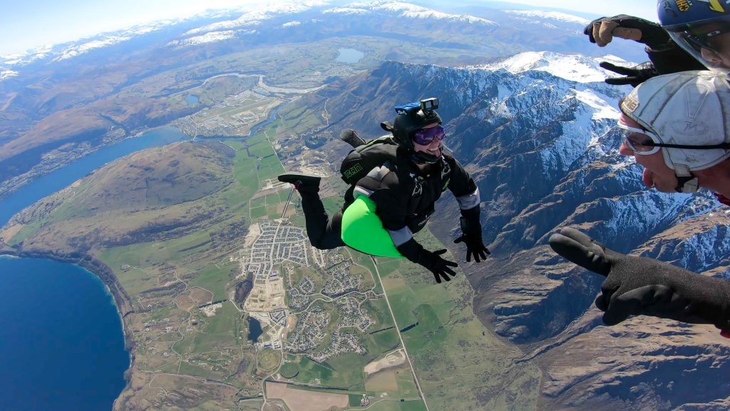 A woman free falling while skydiving and recording tandem skydivers in New Zealand