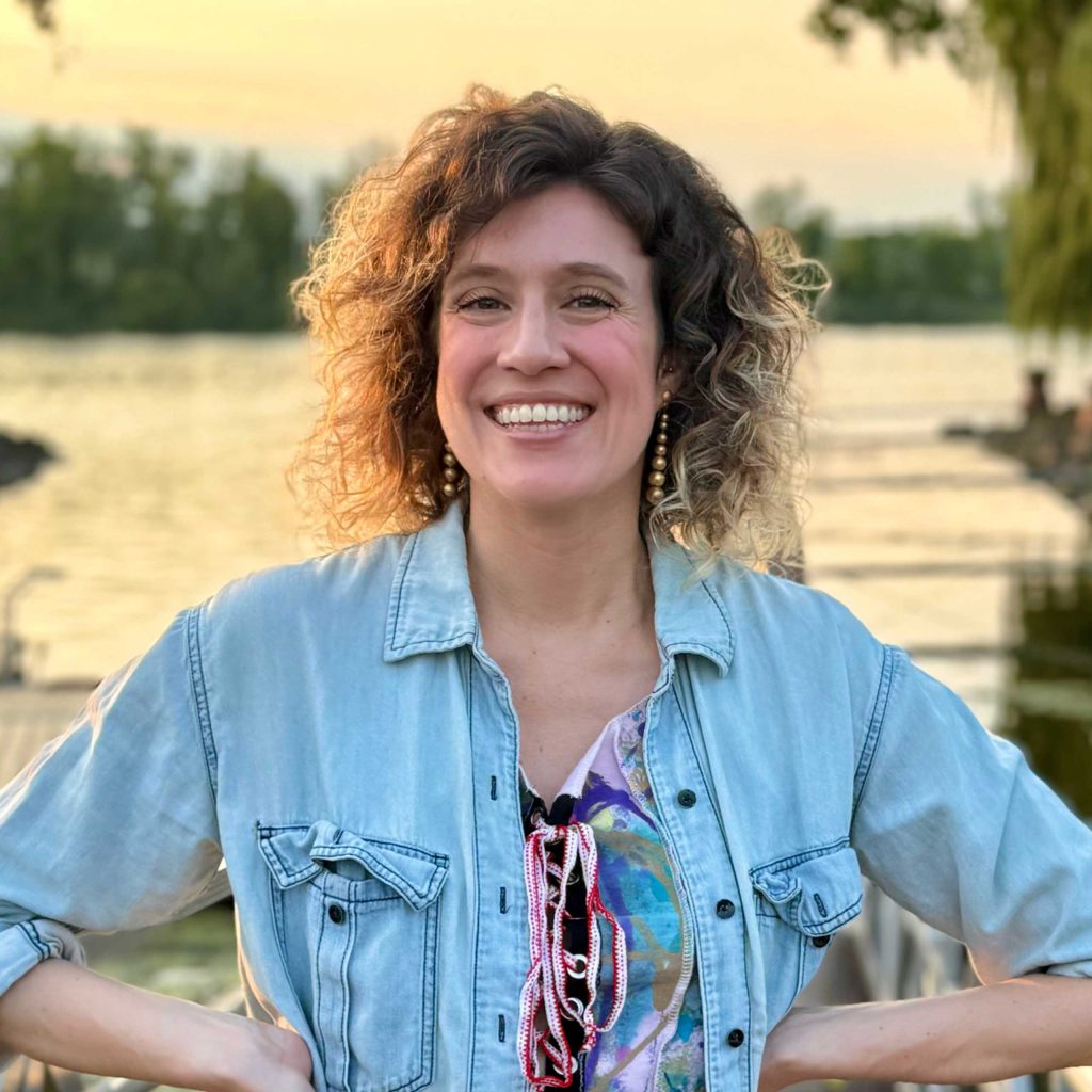 A woman with her hands on her hips and in casual attire with a big smile on her face standing in front of the Hudson River in New York, USA