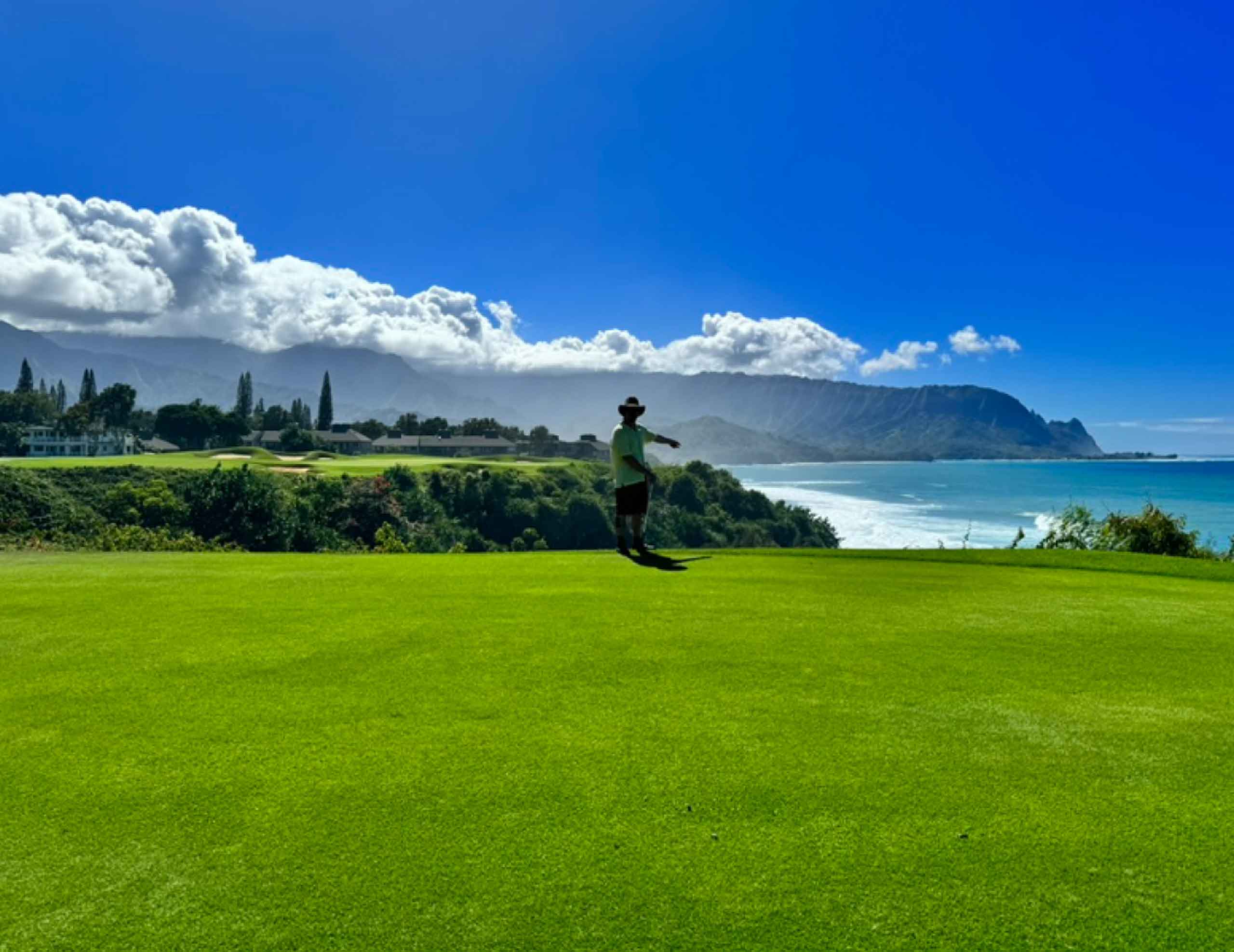 Man golfing with stunning ocean and mountain views behind him at Princeville Makai Golf Club in Kauai, Hawaii, USA